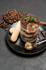 Classic tiramisu dessert in a glass cup and pieces of chocolate on dark concrete background