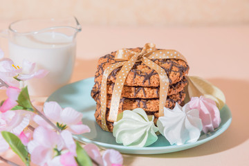 Fresh baked oatmeal crispy cookies on a blue plate on a background of peach color, milk, French multi-colored meringues. Delicious culinary sweet dessert, romantic festive breakfast, food, snacks