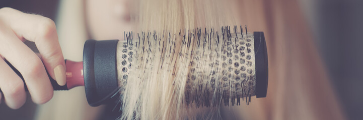 Round brushing in hand combs long blond hair closeup.