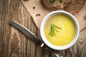 Fresh homemade chicken liver pate in ceramic bowl or ramekin and baguette slices with pate with herbs and garlic on a rustic wooden background. Top view.