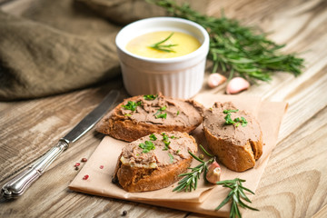 Fresh homemade chicken liver pate in ceramic bowl or ramekin and baguette slices with pate with herbs and garlic on a rustic wooden background