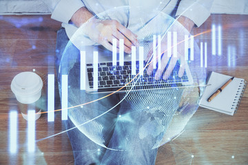 Double exposure of businessman's hands with laptop and stock market graph background. Concept of research and trading.
