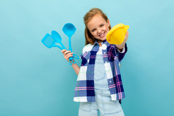 cheerful european girl holding a oven mitts and cutlery in hands on a light blue background