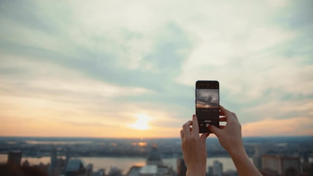 Female hands with a phone taking photo of sunset