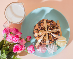 Fresh baked oatmeal crispy cookies on a blue plate on a background of peach color, milk, French multi-colored meringues. Delicious culinary sweet dessert, romantic festive breakfast, food, snacks
