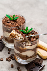 Classic tiramisu dessert in a glass cup, savoiardi cookies and pieces of chocolate on concrete background