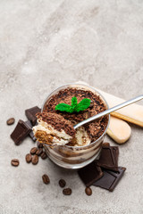 Classic tiramisu dessert in a glass cup, savoiardi cookies and pieces of chocolate on concrete background