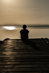 silhouette of man sitting on pier at sunset