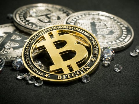 Shiny gold bitcoin virtual currency coin laying on black table with diamonds