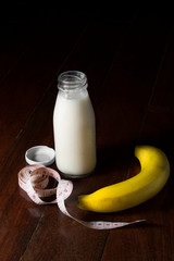 Bottle of milk with banana and measuring tape.