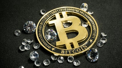 Shiny gold bitcoin virtual currency coin laying on black table with diamonds