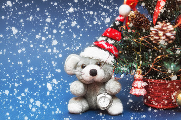A little fluffy rat in a Christmas hat. Nearby is a festive Christmas tree with toys on a blue background. Happy new year 2020 rats. Merry Christmas! Blank space for text. Mock up