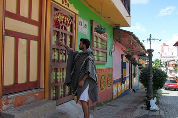 Man with poncho knocking on the door of his colorful house
