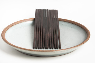 Six Pairs Of Sculptural Black Chopsticks On Stoneware Plate