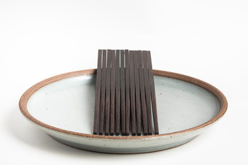 Six Pairs Of Sculptural Black Chopsticks On Stoneware Plate