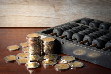 Money coins with old wooden abacus on table.