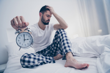 Portrait of his he nice attractive sad lazy tired bearded guy sitting on bed holding in hand alarm...