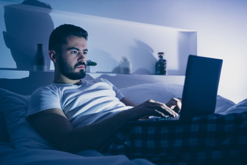 Portrait of his he nice attractive focused bearded guy lying on bed using digital laptop blogging at night late evening home dark room flat house