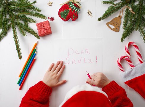 Child writes the letter to Santa Claus. Child's hands, the sheet of paper, pencils and Christmas decorations on a wooden surface. Concept of New year and Christmas. Top view