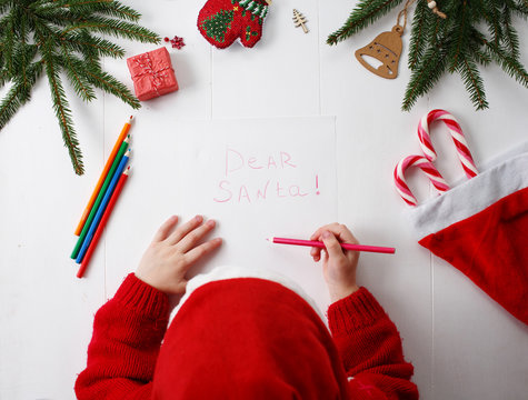 Child writes the letter to Santa Claus. Child's hands, the sheet of paper, pencils and Christmas decorations on a wooden surface. Concept of New year and Christmas. Top view