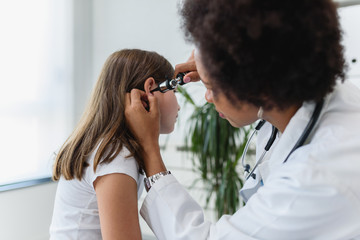 Woman afro american doctor general practitioner examining ear of a ill child. Ear infections. - Powered by Adobe