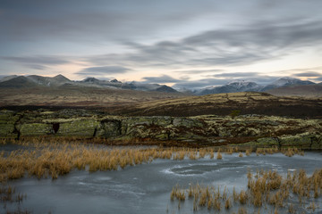 Tranquil scenery with frozen lake, snow covered mountains and fast moving skies over rondane national park in norway. Outdoors and blue hour theme.