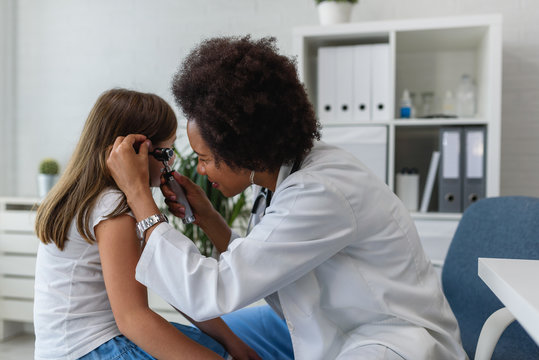 Woman afro american doctor general practitioner examining ear of a ill child. Ear infections.