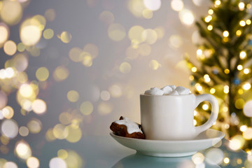 Obraz na płótnie Canvas Hot beverage with marshmalows, gingerbread cookie star shape, bokeh, christmas tree background. Happy New Year, card concept. Close-up, copy space