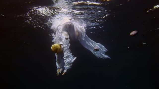 Young woman free diver underwater model angel in white cloth and cameraman. Creativity and art of creating images on background of blue water.