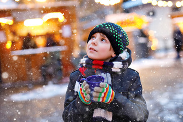 Little cute kid boy drinking hot children punch or chocolate on German Christmas market. Happy child on traditional family market in Germany, Laughing boy in colorful winter clothes