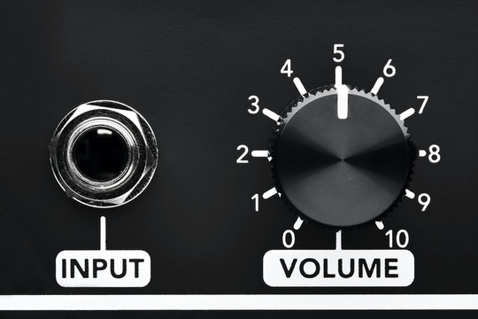 Close up detail of volume control knob and input jack of a black guitar amplifier