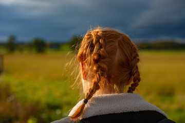 Girl With Red Hair in Braids Walks Through a Field in the Countryside