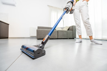 Woman cleaning floor with cordless vacuum cleaner in the modern white living room. Concept of easy...