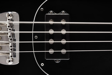 Close up detail of a black bass guitar pickups, frets and bridge