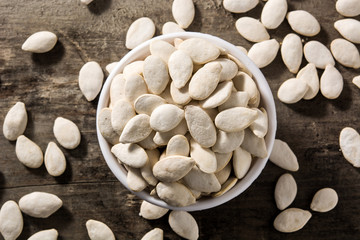 Pumpkin seeds in white bowl on wooden background. Top view. 