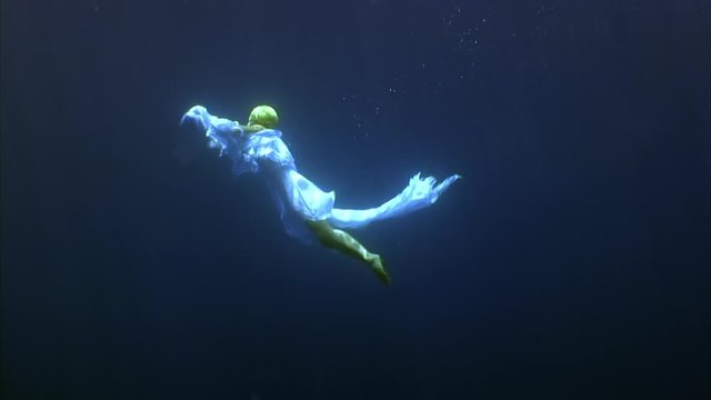 Young woman free diver underwater model angel in white cloth. Creativity and art of creating images on background of seabed.