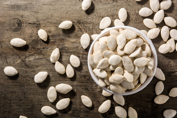 Pumpkin seeds in white bowl on wooden background. Top view. Copy space