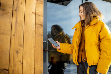 Woman locking smartlock on the entrance door using a smart phone. Concept of using smart electronic...