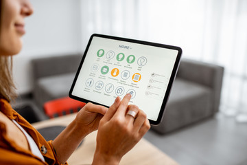 Young woman controlling home with a digital touch screen panel. Concept of a smart home and mobile application for managing smart devices at home