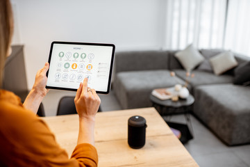 Young woman controlling home with a digital touch screen panel. Concept of a smart home and mobile...