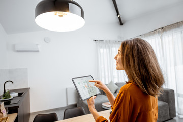 Young woman controlling home light with a digital tablet in the living room. Concept of a smart...