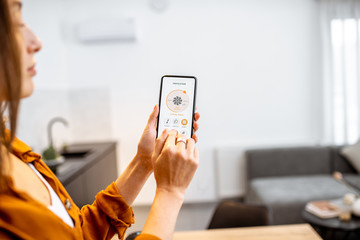 Woman controlling home ventilation or conditioning with a smart phone. Concept of a smart home and...