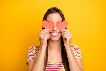 Closeup photo of funny lady holding hands little red paper hearts shy person hiding eyes flirty girlish mood wear casual striped t-shirt isolated yellow color background