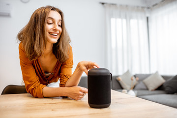 Young woman turning on wireless smart column at home. Concept of a smart home wireless devices. Concept of smart home and voice command control - obrazy, fototapety, plakaty