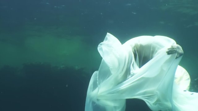 Young woman underwater model in white cloth on background of blue water. Concept of creativity and art of creating images.