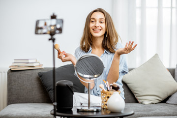 Young woman recording on a smart phone her vlog about cosmetics, showing and demonstrating makeup....