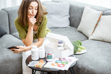 Thoughtful woman with nutritional supplements at home. Concept of individual online selection of...