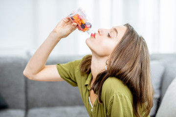 Woman taking vitamins or nutritional supplements in the form of pills while sitting on the couch at home. Concept of biohacking and preventive medicine