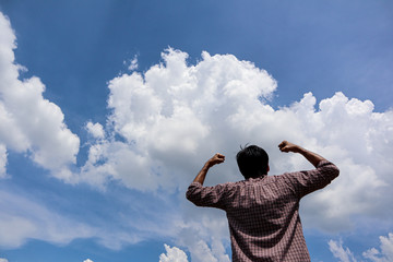 A man looking into the blue sky with white cloud   holding arms up