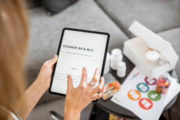 Woman checking the result of medical tests on a digital tablet, close-up with nutritional supplements on the background. Concept of individual online selection of food supplements